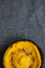 Chickpea yellow hummus with cumin and olive oil served in ceramic dark bowl in grey background. Arabian traditional food. Vegan vegetarian healthy dinner