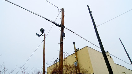 A yellow box low-rise building with window, fire escape, and chimney, flanked by three wooden pole lines.