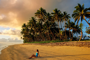 Young woman sitting on a beach at sunrise  in Lavena village on Taveuni Island, Fiji