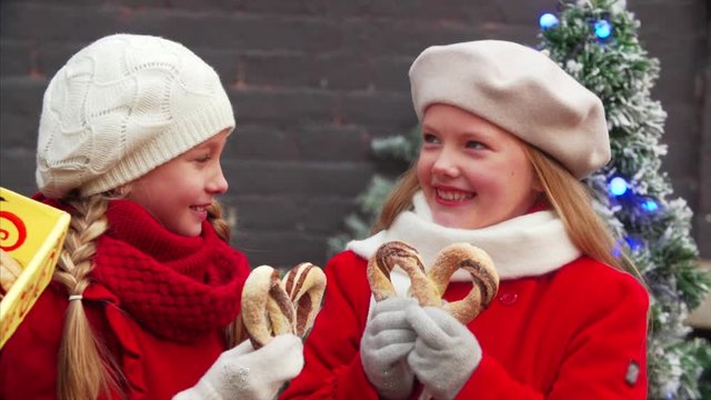 Portrait of two cute sisters in red coats holding cracknels and laughing. Christmas decorations