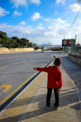 Little tourist boy in red jacket hitch-hiking on the Malta road