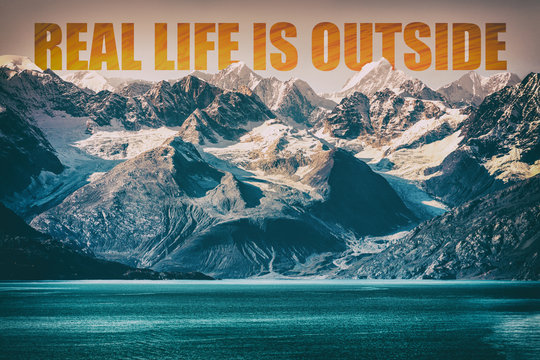 REAL LIFE IS OUTSIDE motivational quote on mountain range landscape background. Adventure message to inspire people to travel in nature. Snow capped peaks background of Alaska. USA.