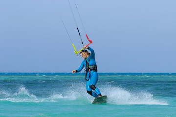 Kite surfing girl in sexy swimsuit with kite in sky on board in blue sea riding waves with water splash. Recreational activity, water sports, action, hobby and fun in summer time. Kiteboarding sport