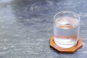 Glass of cool water with wood coaster on gray stone table in coffee shop.