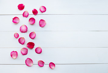 Rose petals on white wooden background.