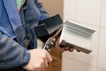 Closeup professional workerman in blue dirty uniform cut aluminum profile with metal scissors, cutter. Concept construction site and renovation in the kitchen of restaurant