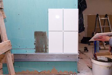 Closeup repair, white ceramic tile with adhesive on drywall in bathroom, professional builder man's hand. Concept renovation repair, overhaul, contract tiler, team of construction, repairman