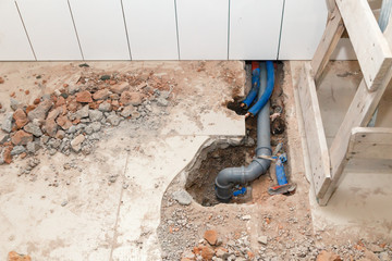 Repair plastic polypropylene gray sewer pipes in the hole in brick floor with broken tiles. Concept...