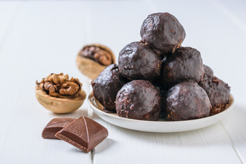 Two pieces of chocolate, two walnuts and homemade dried fruit candies on a white wooden table.