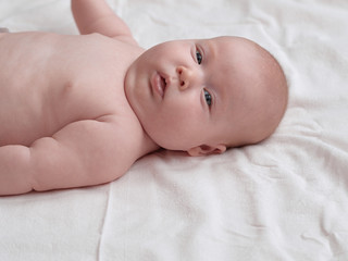 The baby looks with interest in the frame.  The baby lies on a white linen cloth.