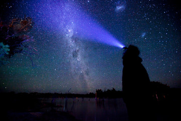 A man in the night looks up at the stars wearing a head torch.