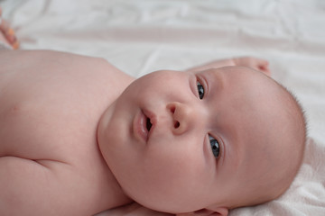 Baby with a surprised face with open mouth. The baby lies on a white linen cloth.