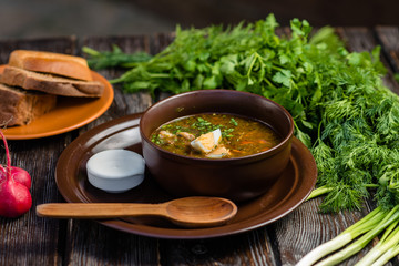 green borsch with egg and sour cream in a clay plate on a wooden table