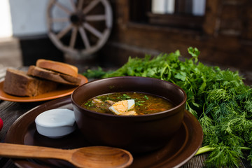 green borsch with egg and sour cream in a clay plate on a wooden table
