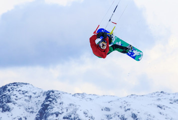 Naklejka na ściany i meble Professional kite boarding rider sportsman with kite in sky jumps high acrobatics kiteboarding trick with grab of kiteboard. Recreational activity, extreme active sports, snow kiting ski snowboard
