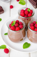 Chocolate pudding (mousse) with fresh raspberries in glass jars on a white wooden background. Dessert on Valentine's Day and Women's Day.
