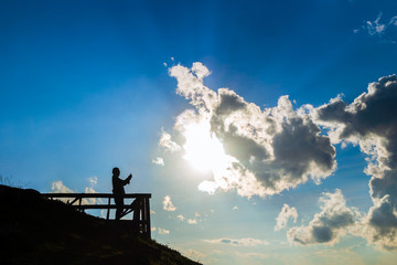 silhouette of man holding smartphone and take a photo of sun and clouds with sky background