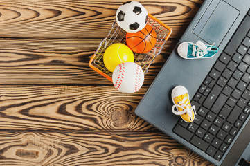 Sports equipment in market basket beside old dirty laptop on brown table with copy space. Online trade concept. Top view
