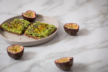 Avocado Kurkuma Vollkorn Sonnenblumenkern Brot und Maracuja zum Frühstück auf Marmor Hintergrund