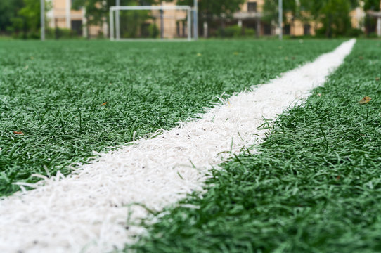 Artificially turfed football field with green grass and white line, close-up view
