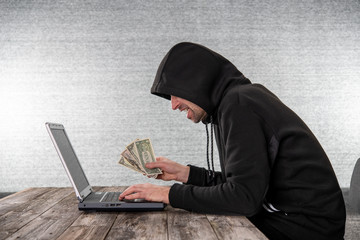 hacker in black hoody with laptop and dollar notes