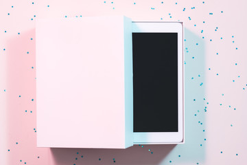 Tablet computer present. White box on pink confetti background. Portable technology