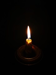 Burning candle in a candlestick on a black background