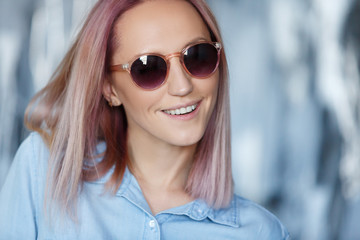 Close-up portrait of a charming hipster student in sunglasses with pink hair in a jersey shirt. Cute young girl in stylish modern clothes posing in studio