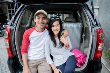 couple sitting on a car's trunk smiling together 