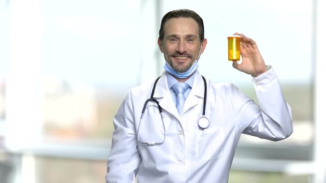 Cheerful doctor showing bottle of pills. Smiling health care specialist with stethoscope presenting yellow unlabeled bottle with medication.