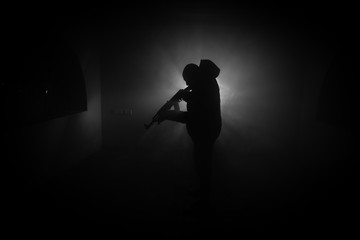 Silhouette of man with assault rifle ready to attack on dark toned foggy background or dangerous...