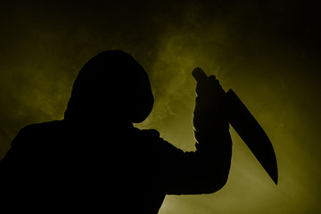 A dangerous hooded man standing in the dark and holding a knife. Face can not be seen. Committing a...