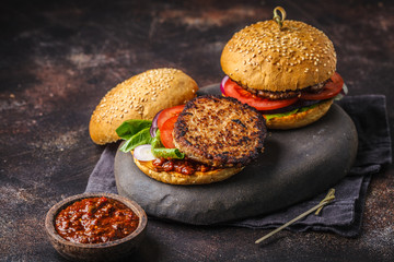 Traditional burgers with meat, sauce and vegetables on a dark background.