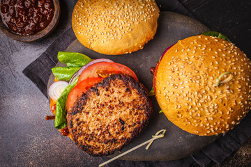 Traditional burgers with meat, sauce and vegetables on dark background, top view.