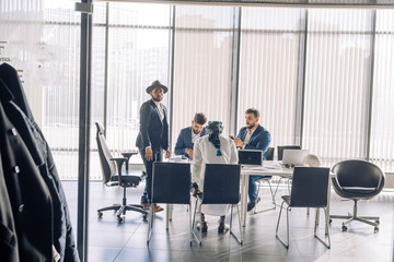 Elegant well-dressed business men of different age and ethnicity in suits gathered together for negotiating, collaborating in spacious modern office meeting room