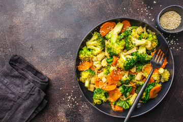 Vegan wok stir fry with broccoli and carrot in black dish, top view, copy space.