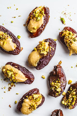Dates stuffed with peanut butter, chocolate and pistachios on white background.