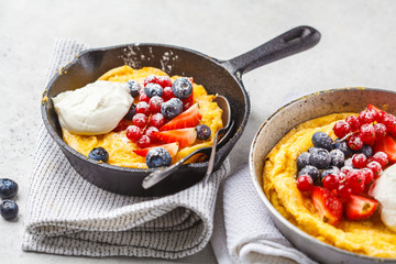 Dutch baby pancake with berries and cream in a cast-iron pan.