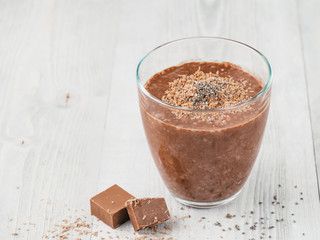 Chocolate chia pudding in glass and chocolate cubes slice on gray wooden table. Healthy vegan...