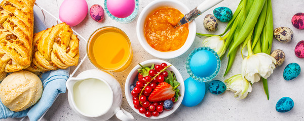 Easter Breakfast table, top view. Colored eggs, flowers, buns, milk, juice and jam, white background.