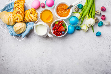 Easter Breakfast table, top view. Colored eggs, flowers, buns, milk, juice and jam, white background.