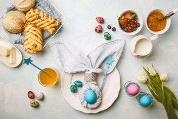 Easter Breakfast table. Colored eggs, bun, juice and jam. Blue background, top view, flat lay.