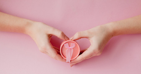 Round pink gift box in women's hands on a pink background. Festive concept for Valentine's day, Mother's day or birthday
