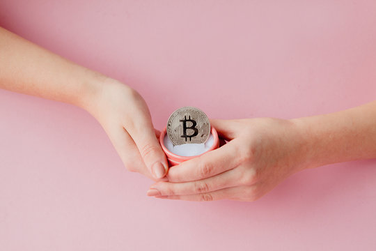Woman's hands holding bitcoin in pink gift box on a pink background, symbol of virtual money