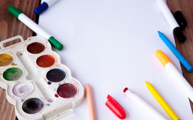 A white sheet of paper lay on a wooden table, near , pencils, paints and markers. Back to school....