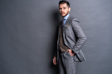 Obraz premium A confident elegant handsome young man standing in front of a grey background in a studio wearing a nice suit.