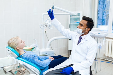 Male asian dentist in dental office talking with female patient and preparing for treatment.