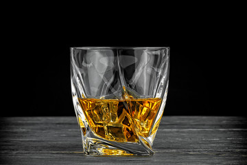 Glass of whiskey with ice cubes on wooden background