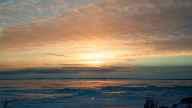 Time lapse loop of dramatic sunrise clouds moving in two directions over icy bay.