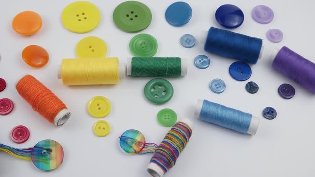 Composition of the sets of colorful buttons and spools of colorful thread are stacked in the spectrum of the colors of the rainbow on the white the background